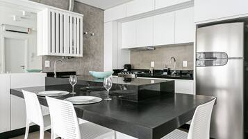 A modern kitchen with white cabinets, a stainless steel refrigerator, and a black countertop island with white chairs.