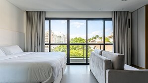 A modern hotel room with a large window, a bed, a sofa, and a view of the city. - ZEE Studios by Viva - Studios a 200m da beira-mar norte (Florianópolis)