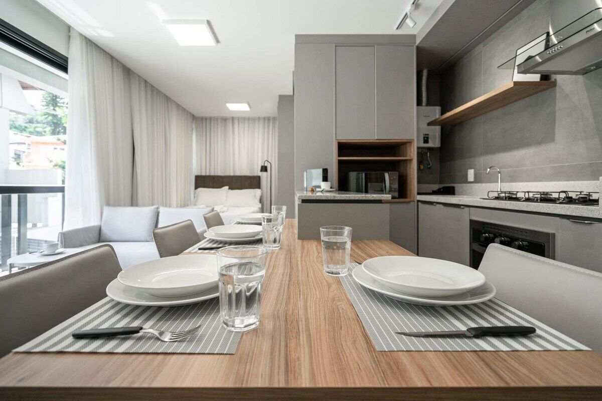 A modern hotel room with a dining area, kitchenette, and a balcony with curtains.