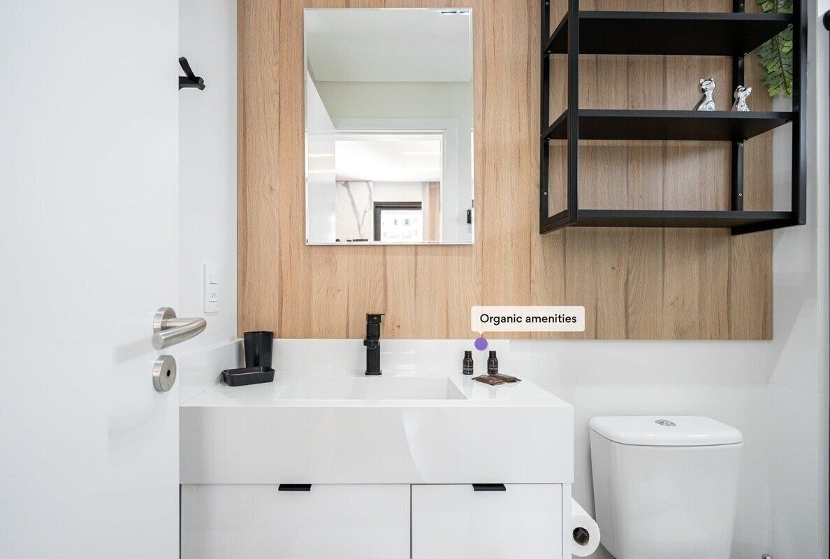 Un baño moderno con un tocador blanco, un panel de pared de madera, un estante negro con adornos y un inodoro.