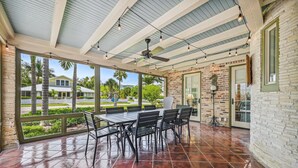 A covered patio with a brick wall, a table with chairs, and a ceiling fan.