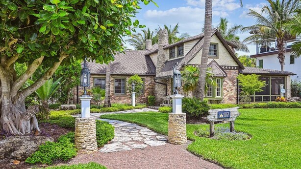 A two-story house with a stone facade, a stone pathway leading to the entrance, and a well-maintained lawn.