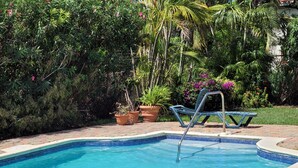 A swimming pool with a blue tiled edge, surrounded by lush greenery and potted plants. - Relaxing, Amazing beach, pool, Cheap cars, quiet area, surfers paradise 3 (Christ Church)