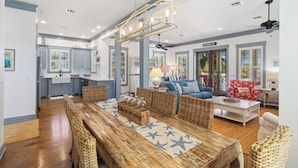 A spacious living room with a large wooden dining table, wicker furniture, and a ceiling fan. - THE GOOD STUFF IS A LUXUROUS 3BD HOME W/COMMUNITY POOL, GATED COMMUNITY! (Port Saint Joe)