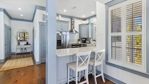 A modern kitchen with a central island, bar stools, and a large window with blinds. - THE GOOD STUFF IS A LUXUROUS 3BD HOME W/COMMUNITY POOL, GATED COMMUNITY! (Port Saint Joe)