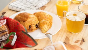 Disposição de café da manhã com croissants, suco de laranja e café em mesa de madeira.