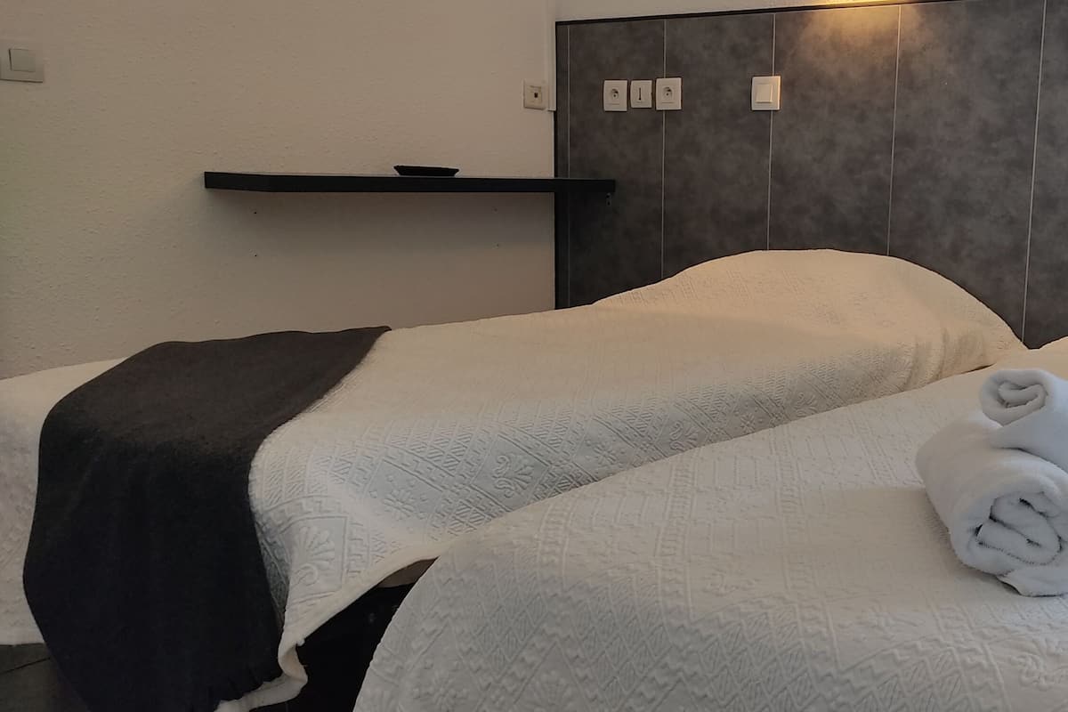 A hotel room with two beds, a dark headboard, a shelf with a bowl, and a rolled towel on one bed.