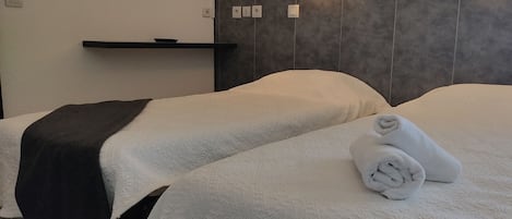 A hotel room with two beds, a dark headboard, a shelf with a bowl, and a rolled towel on one bed.