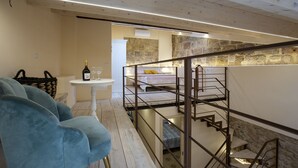 A modern interior with a staircase, a bed, a small table with a bottle and glasses, and a blue chair. - The Theater Suite: Comfort, Position and lots of Light (Alghero)