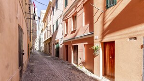A narrow cobblestone street flanked by buildings with balconies and shutters. - The Theater Suite: Comfort, Position and lots of Light (Alghero)