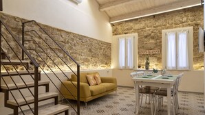 A staircase leading to a living area with a stone wall, a yellow sofa, a dining table with chairs, and a window with curtains. - The Theater Suite: Comfort, Position and lots of Light (Alghero)