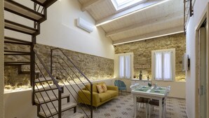 A spacious room with a stone wall, a yellow sofa, a dining table with chairs, and a staircase with a metal railing. - The Theater Suite: Comfort, Position and lots of Light (Alghero)
