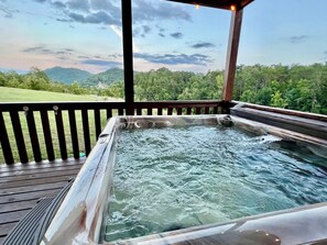 Een hottub met een houten terras en uitzicht op een bebost heuvelgebied.