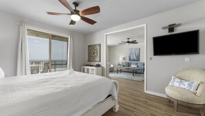 Una camera da letto con un letto grande, ventilatori a soffitto, televisore e un balcone con tende.