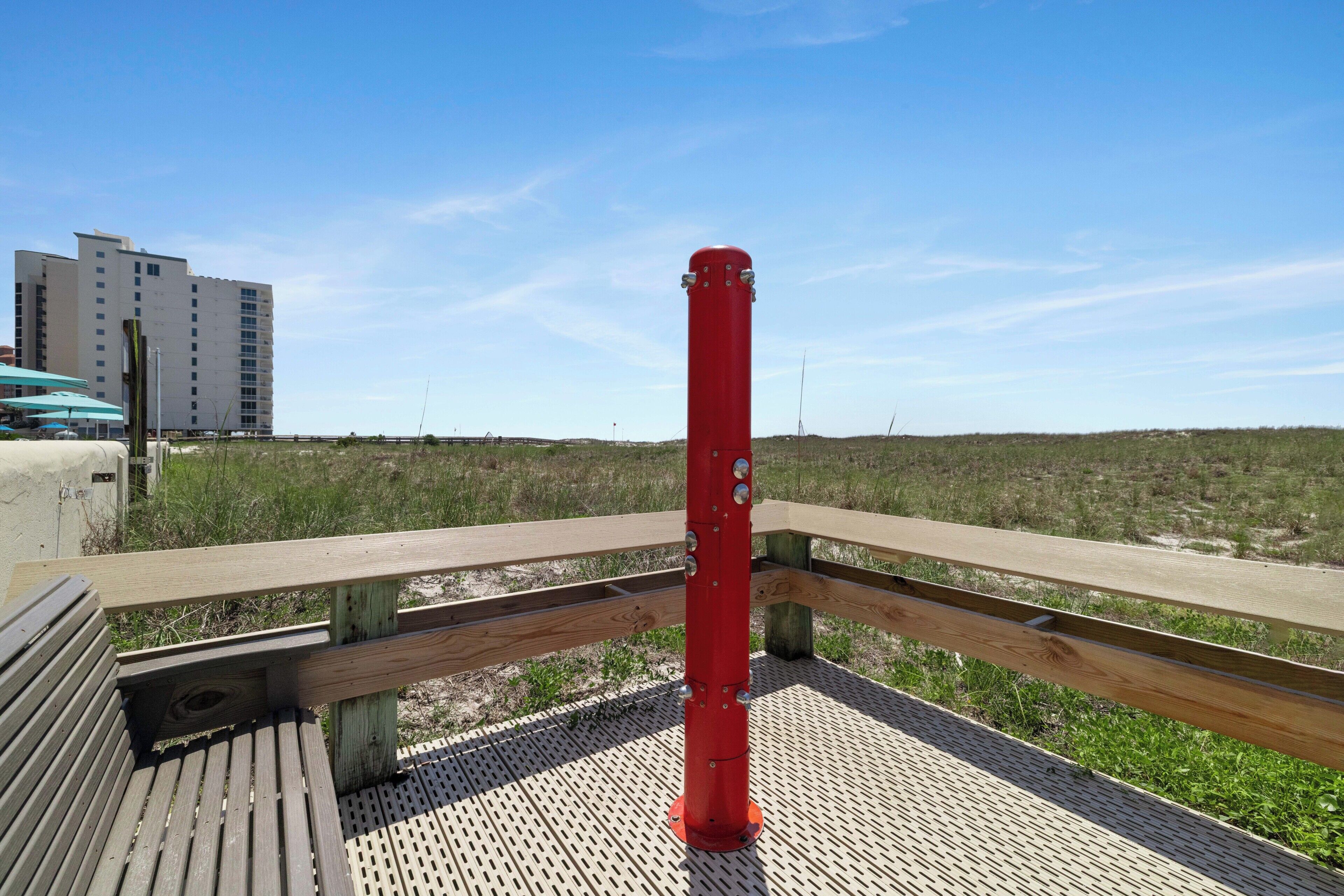 Um deck de madeira com um mastro vermelho, um edifício ao fundo e uma área gramada.