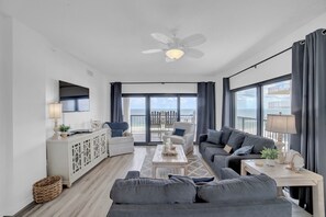 Een ruime woonkamer met een plafondventilator, een groot raam met uitzicht op de oceaan en een balkon met buitenmeubilair.