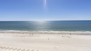 A beach with a clear sky, calm sea, and a few people walking along the shore. - Island Royale 903 by Liquid Life (Gulf Shores)