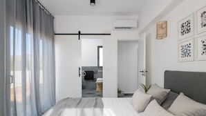 A modern bedroom with a bed, curtains, and a view into the bathroom. - Seasand Villa (Rhodes)