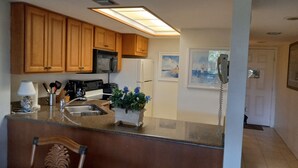 A kitchen with wooden cabinets, a microwave, a refrigerator, a sink, and a telephone. - Near beach, view tropical plantings from 4th floor privacy, + pickleball courts! (Naples)