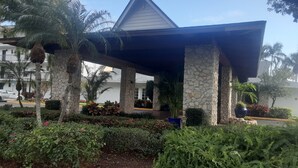 A covered outdoor area with stone pillars, surrounded by lush greenery and flowering plants. - Near beach, view tropical plantings from 4th floor privacy, + pickleball courts! (Naples)