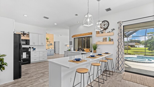 A modern kitchen with a central island, bar stools, and a view of a swimming pool. -  Large pool/spa home minutes from beach with arcade games and canal for fishing. (Bradenton)