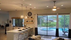 A modern kitchen with a central island, bar stools, and a dining area with a view of a backyard and pool. -  Large pool/spa home minutes from beach with arcade games and canal for fishing. (Bradenton)