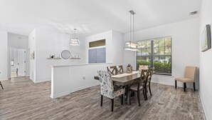 A spacious dining area with a wooden table and chairs, a pendant light, and a view of greenery through large windows. -  Large pool/spa home minutes from beach with arcade games and canal for fishing. (Bradenton)