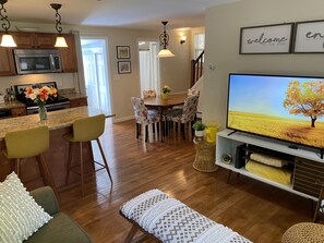 Eine moderne Küche mit Mikrowelle, ein Essbereich mit Tisch und Stühlen, ein Wohnzimmer mit Fernseher und eine Treppe.