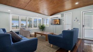 Ein Wohnzimmer mit blauen Sofas, einem Holztisch und einem an der Wand befestigten Fernseher.