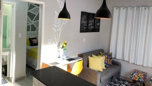 Ein modernes Wohnzimmer mit einer Couch, einem kleinen Tisch und Pendelleuchten. Eine Tür führt in einen anderen Raum.