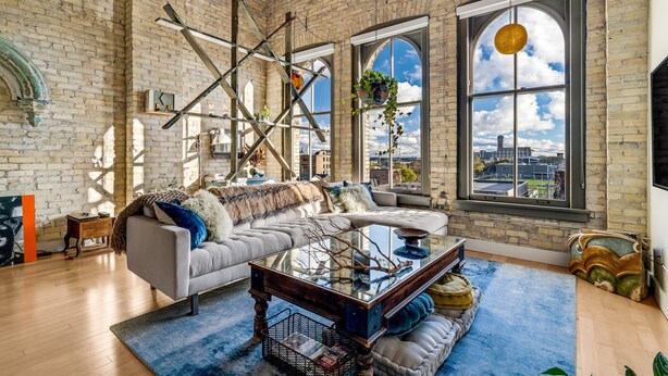 A spacious living room with a large window, a sofa, a coffee table, and a hanging plant. - Cozy 1BD w/ View in Walker's Point, Free Parking (Milwaukee)