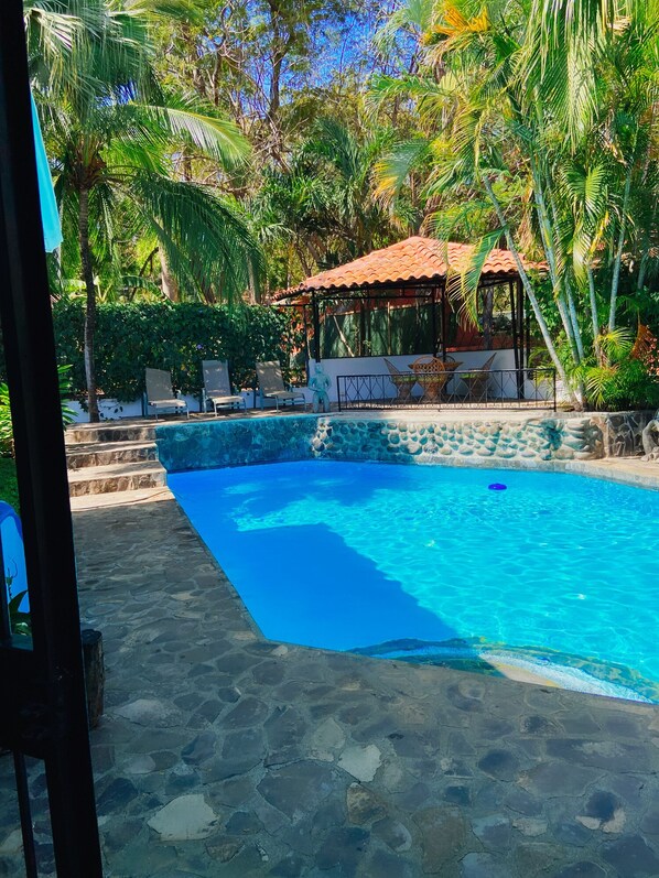 Relax by the serene pool surrounded by lush greenery and a gazebo.