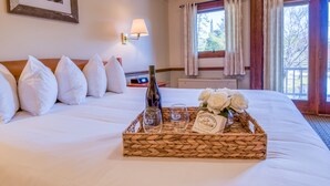 A neatly made bed with white bedding, a bottle of wine, two glasses, and a tray with white roses. - Purity Spring Resort (Madison)
