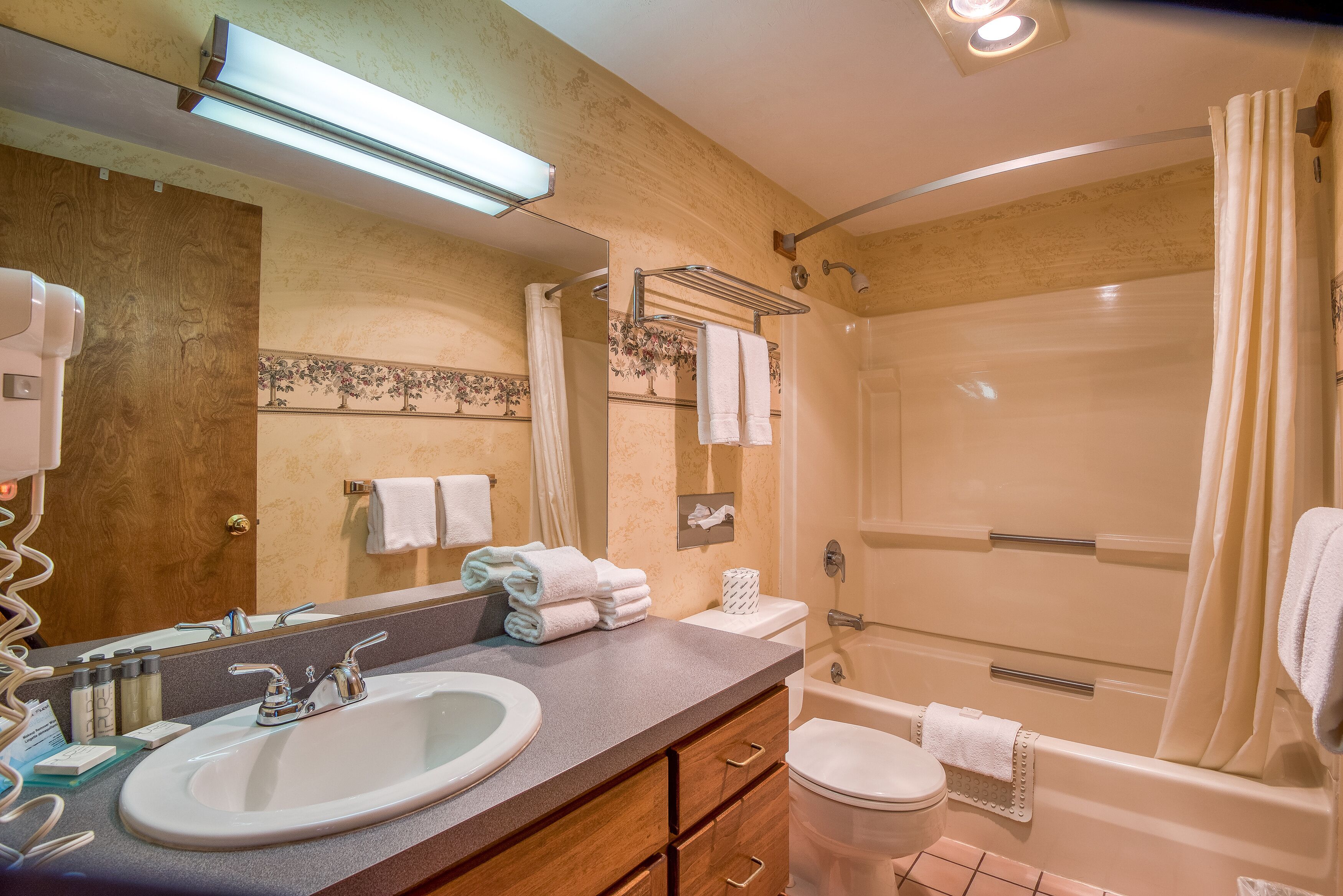 A bathroom with a sink, mirror, towel rack, toilet, and shower.