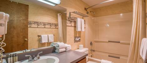 A bathroom with a sink, mirror, towel rack, toilet, and shower.
