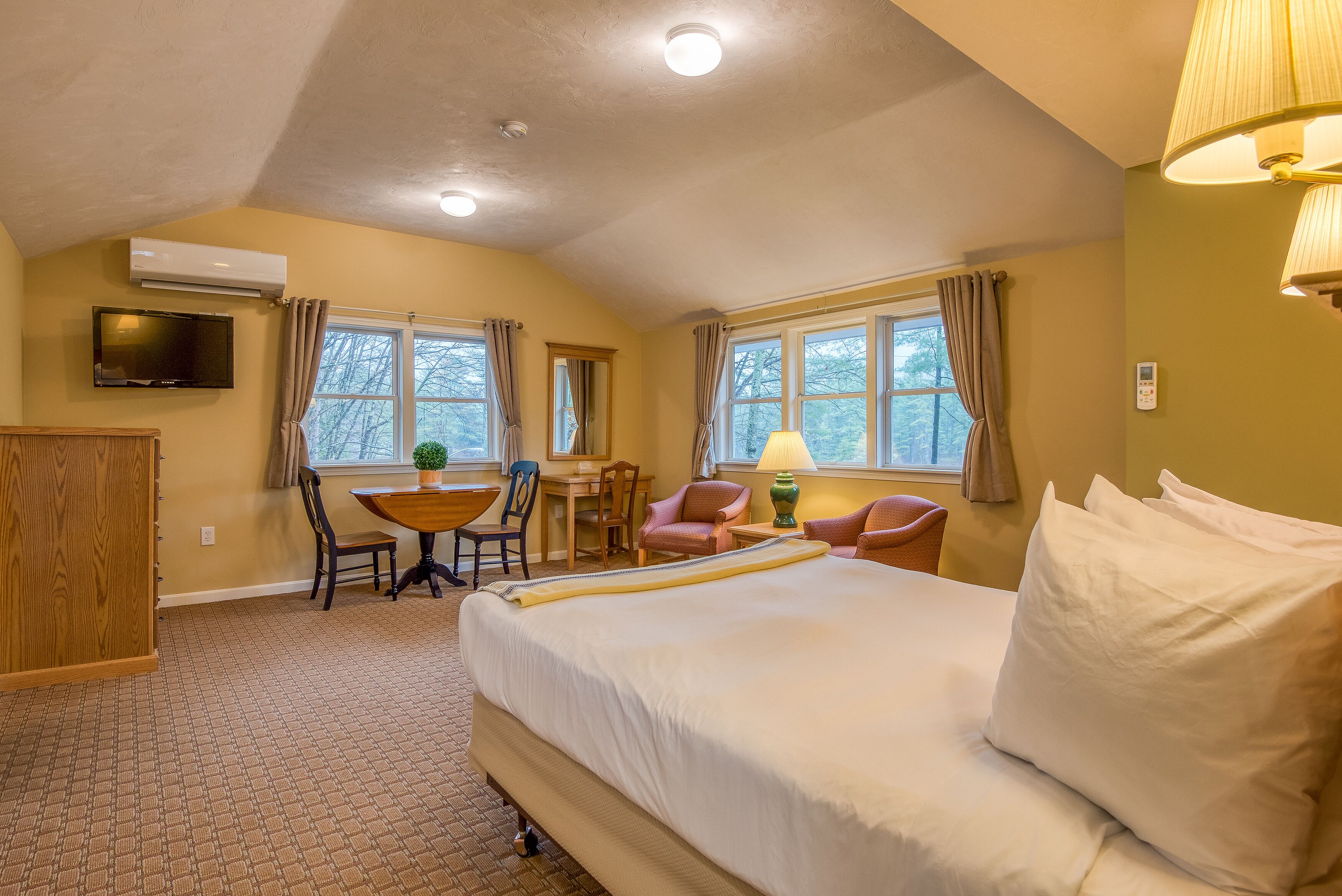 A hotel room with a large bed, a desk with chairs, a television, and windows with curtains.