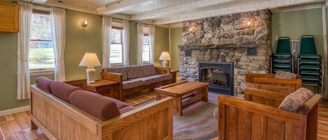 A cozy living room with wooden furniture, a stone fireplace, and a view of the outdoors.