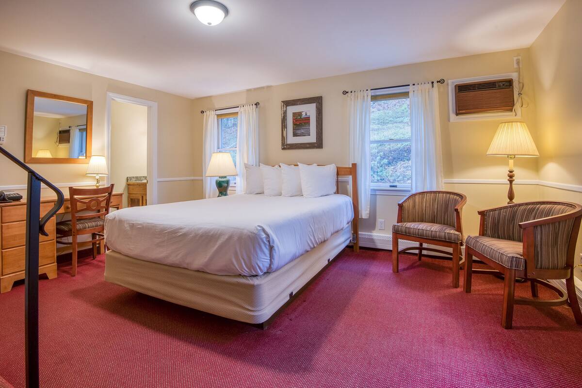 A hotel room with a large bed, two chairs, a desk, and a mirror.