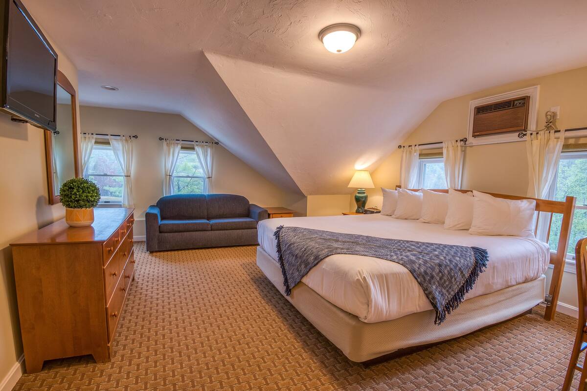 A bedroom with a large bed, a dresser, a TV, a couch, and a window with curtains.