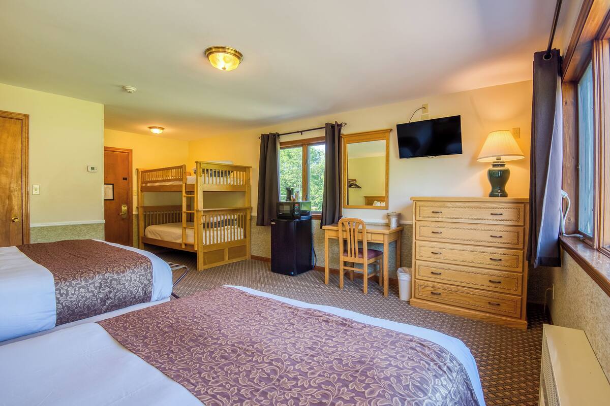 A hotel room with two beds, a desk with a chair, a dresser, a television, and a window with curtains.