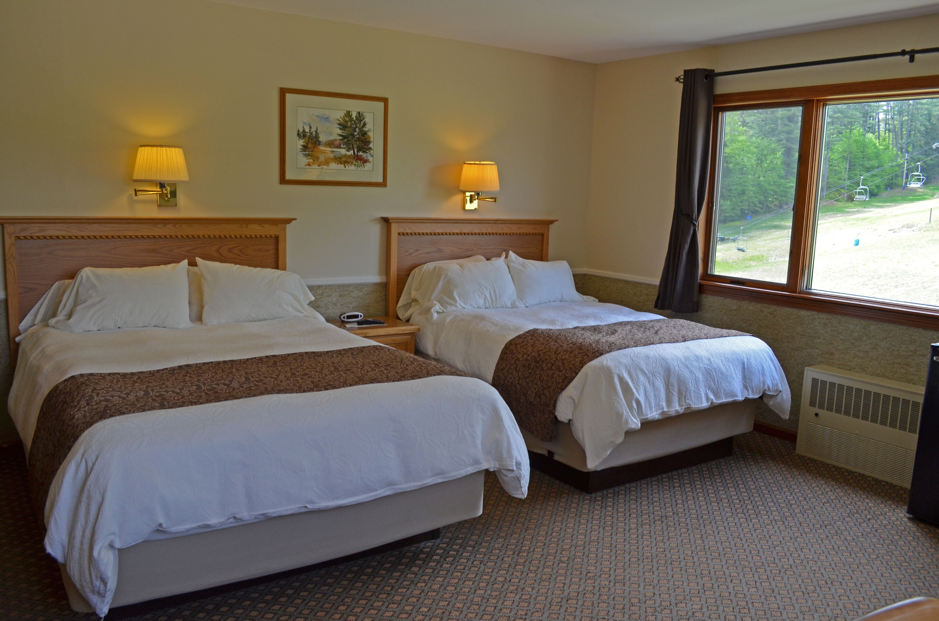 A hotel room with two beds, a window with a view of a ski lift, and a radiator.