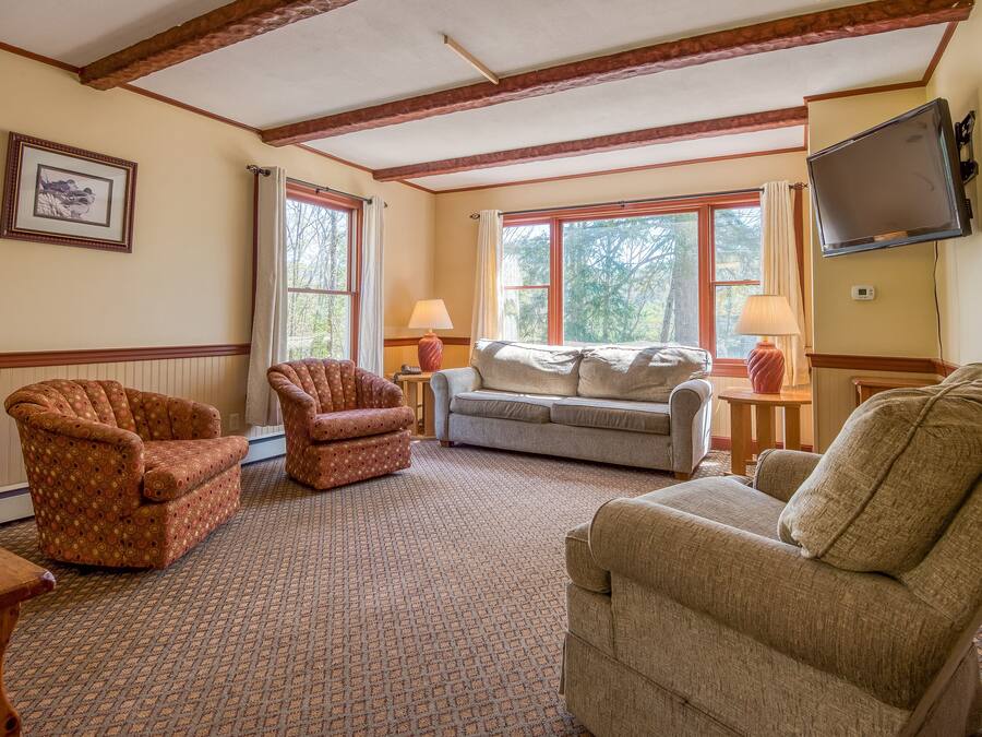 A living room with a patterned carpet, two armchairs, a sofa, and a television mounted on the wall.