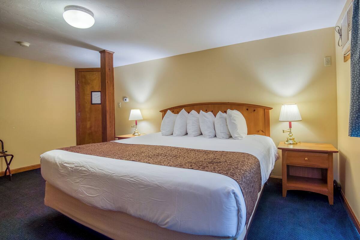 A hotel room with a large bed, two bedside tables with lamps, a wooden headboard, and a door with a picture frame.
