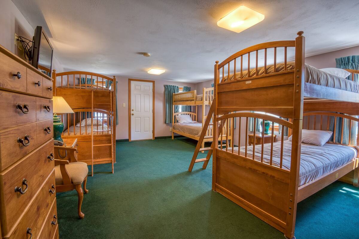 A room with bunk beds, a wooden dresser, and a desk with a lamp.