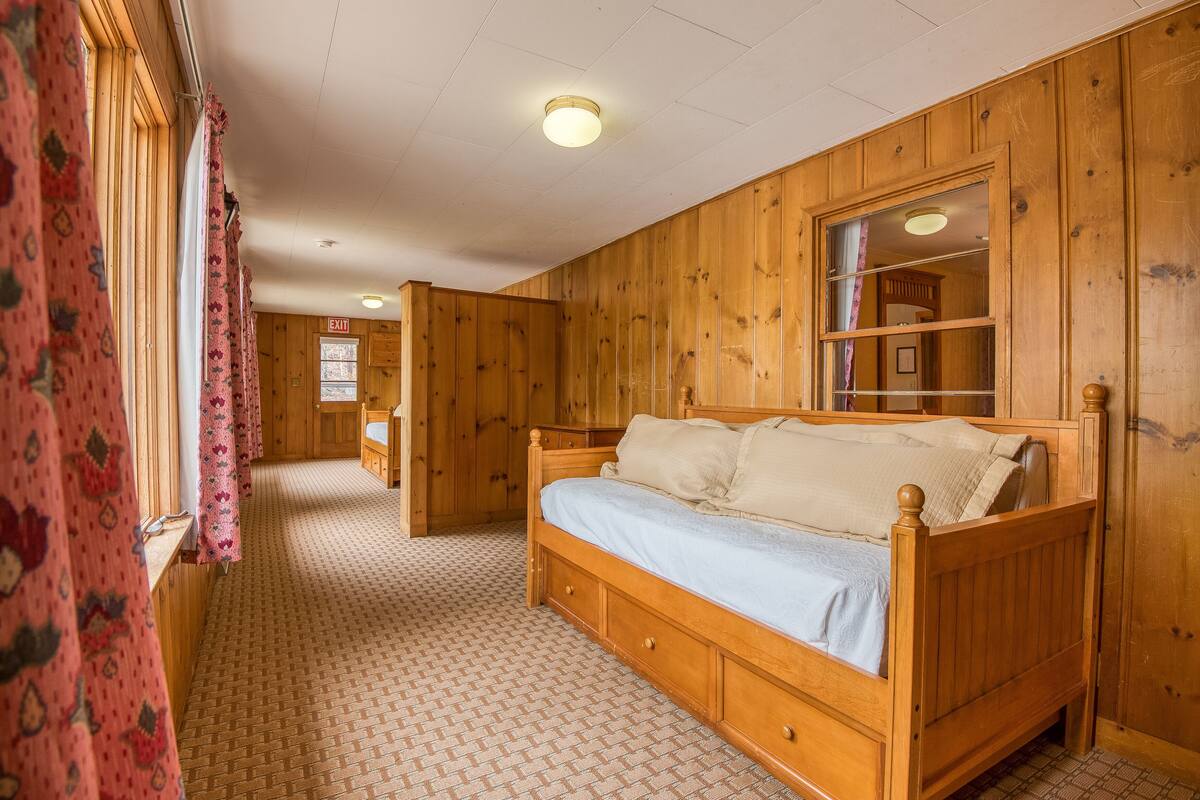 A wooden room with a bed, a window with curtains, and a door with an exit sign.