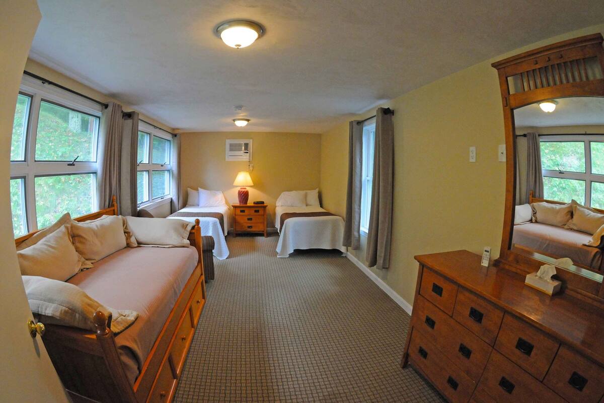 A hotel room with two beds, a wooden dresser, a nightstand, and a window with curtains.