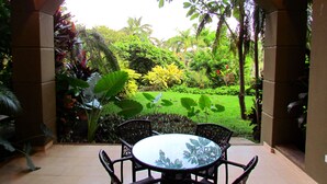 An outdoor patio with a round table and chairs, surrounded by lush greenery and a view of a well-maintained garden. - Condominium 206 Matapalo ideal for family trips and work online.  (Tamarindo)