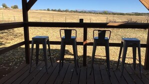 Une terrasse en bois avec trois chaises en métal, donnant sur un champ aride et des montagnes lointaines.