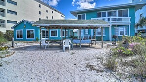 Un patio frente a la playa con sillas de plástico blanco y un área de estar techada.