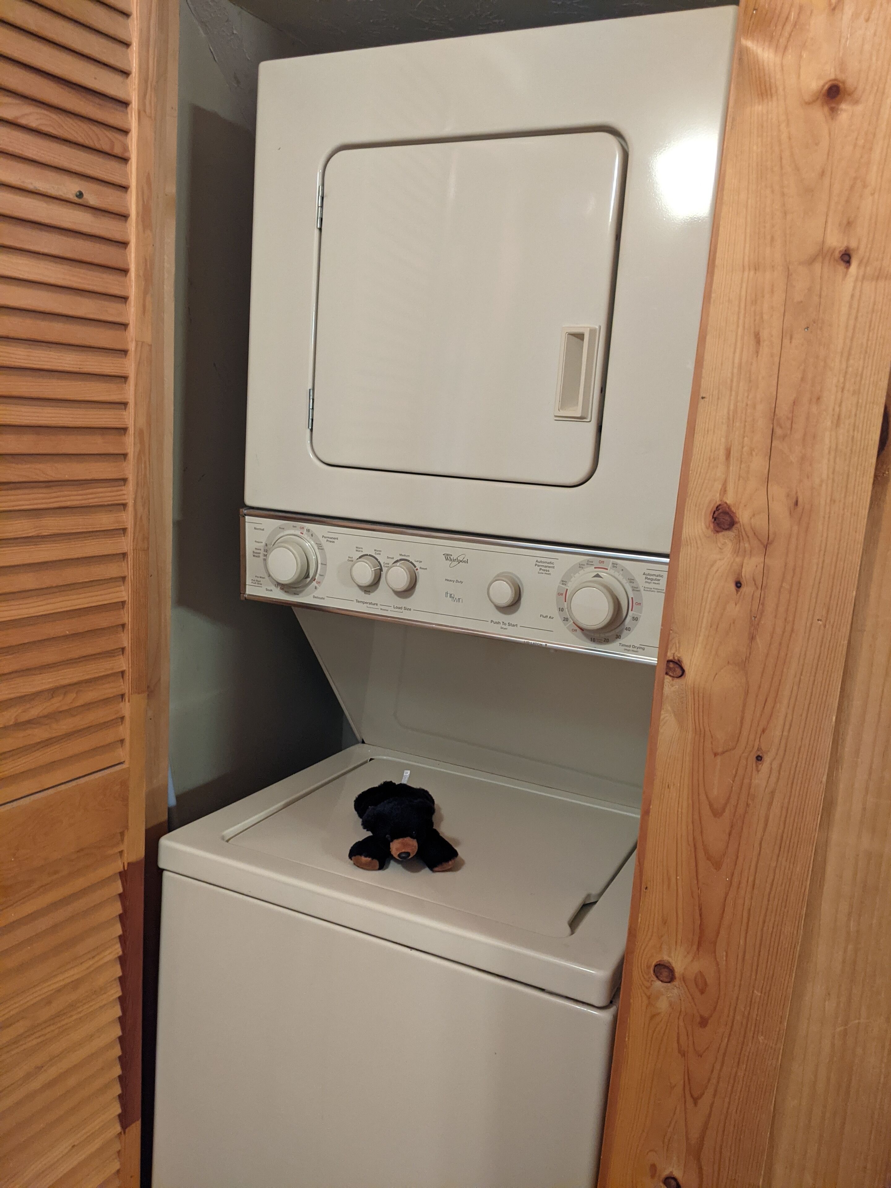 A compact laundry room with a washer and dryer, a wooden door, and a small stuffed toy on the dryer.